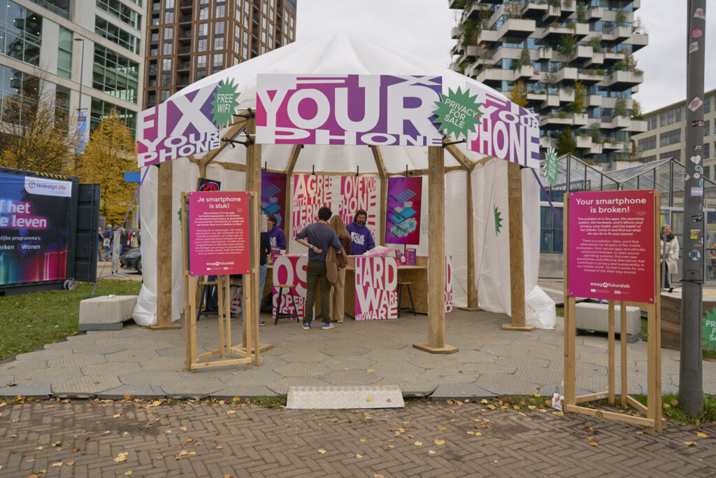 Photograph of people standing inside a dome-like stand that is adorned with large signs that say "Fix Your Phone".